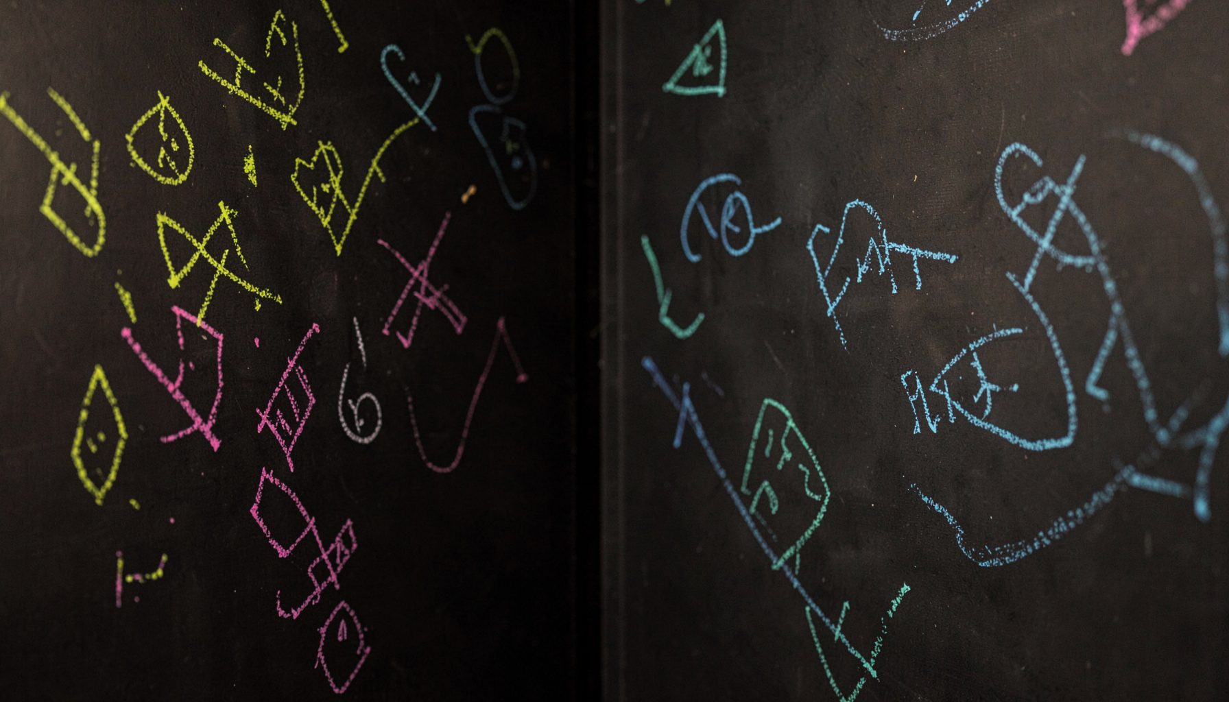 A cozy dark chalkboard-style corner with scattered colorful chalk marks in lime green, magenta, and cyan suggesting handwritten notes