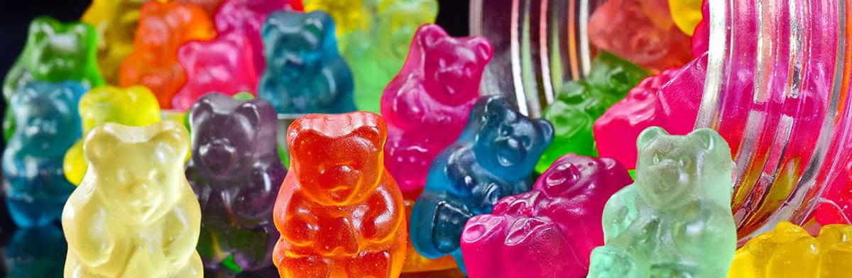 Vivid multicolored gummy bears spilling from a jar in bright saturated red, yellow, green, and blue tones, playful and energetic