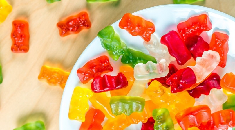 Colorful gummy bear candies on a white plate and wooden surface in vibrant red, orange, yellow, and green tones, playful mood